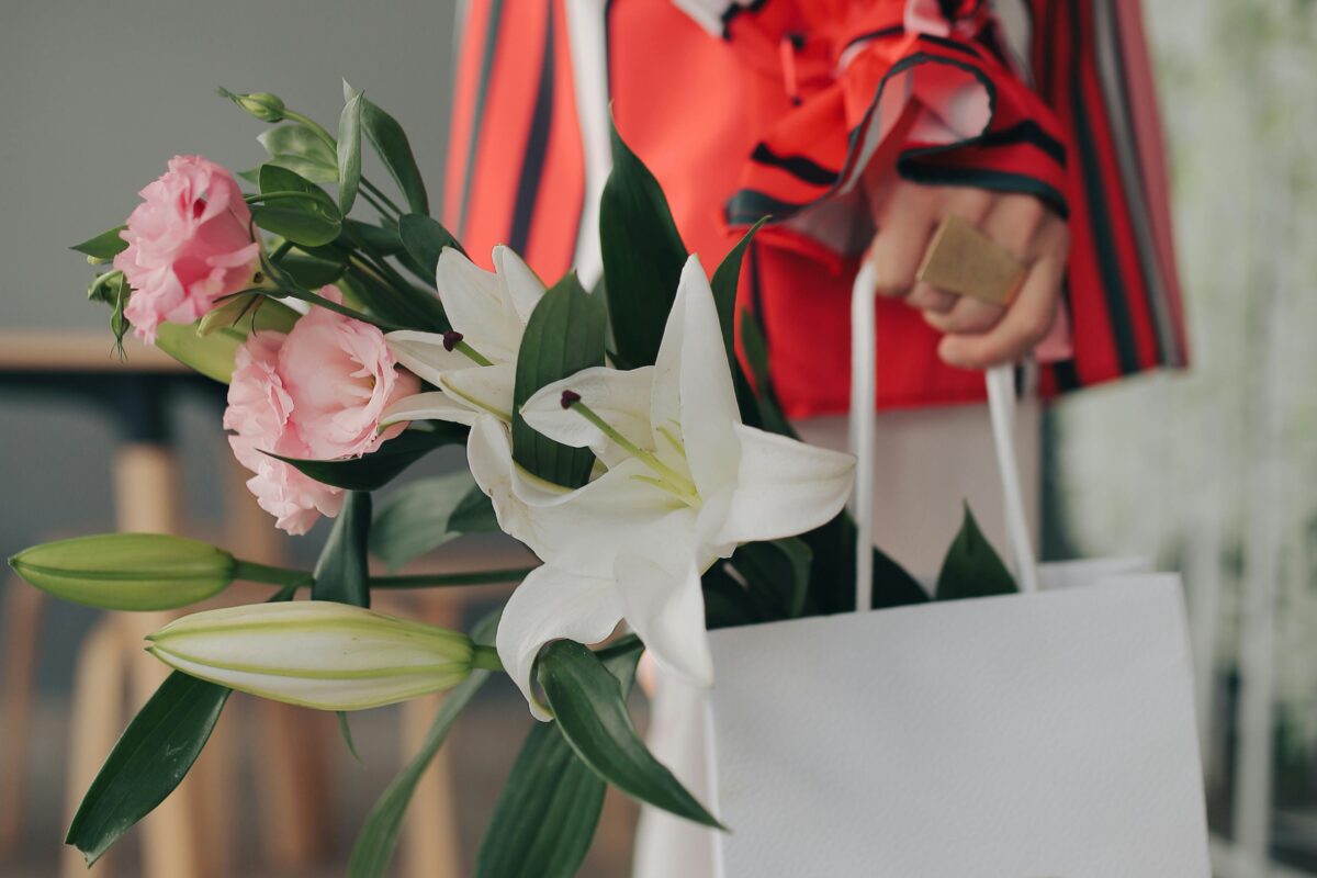 Woman in a colorful outfit holding a Dior bag with lilies and roses.