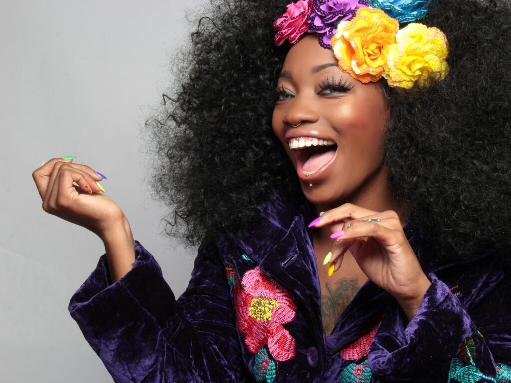 A joyful woman with colorful flowers in her afro, exuding happiness and vibrant style.