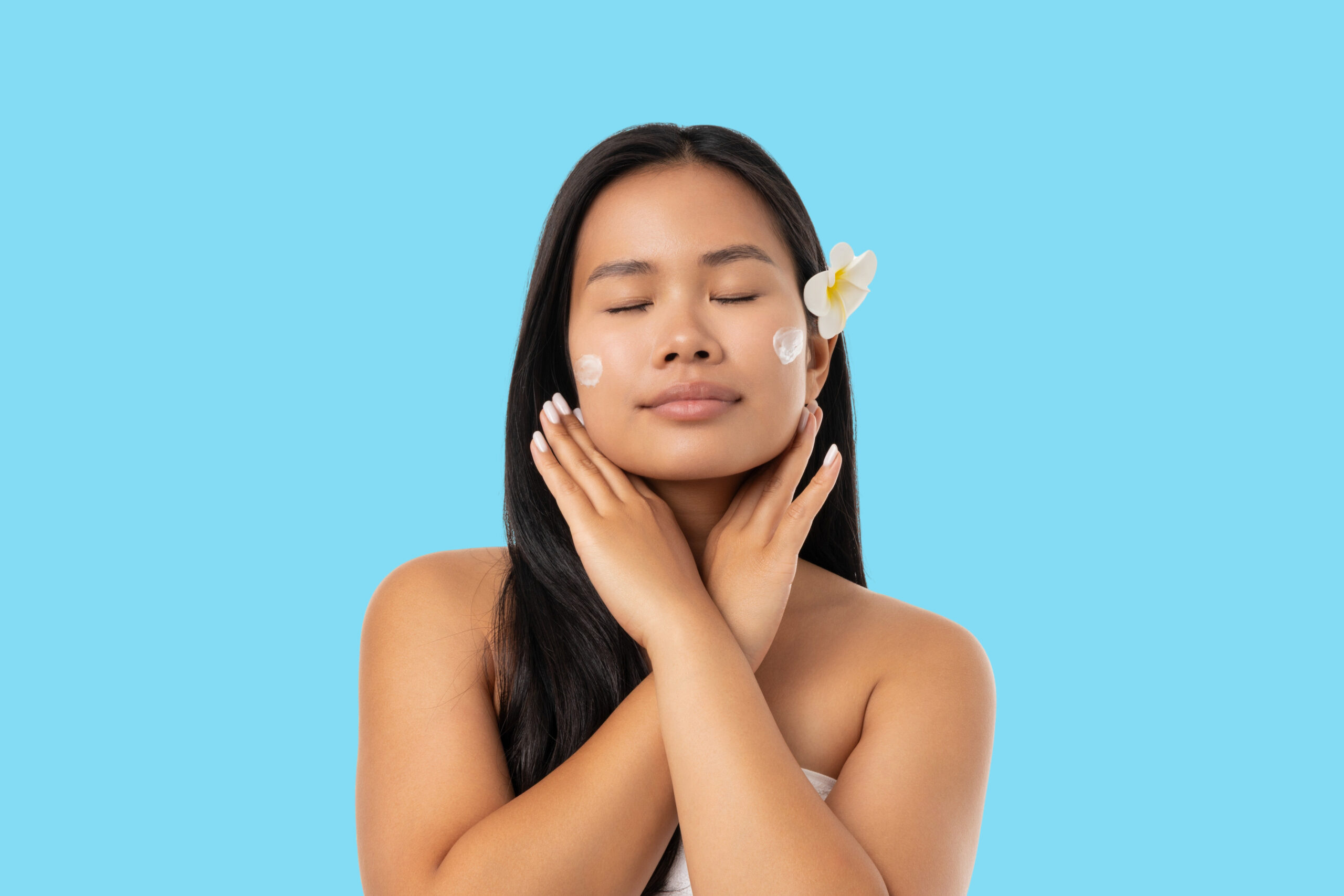 Woman applies cream on her face with closed eyes and a flower. applying body oil before or after lotion